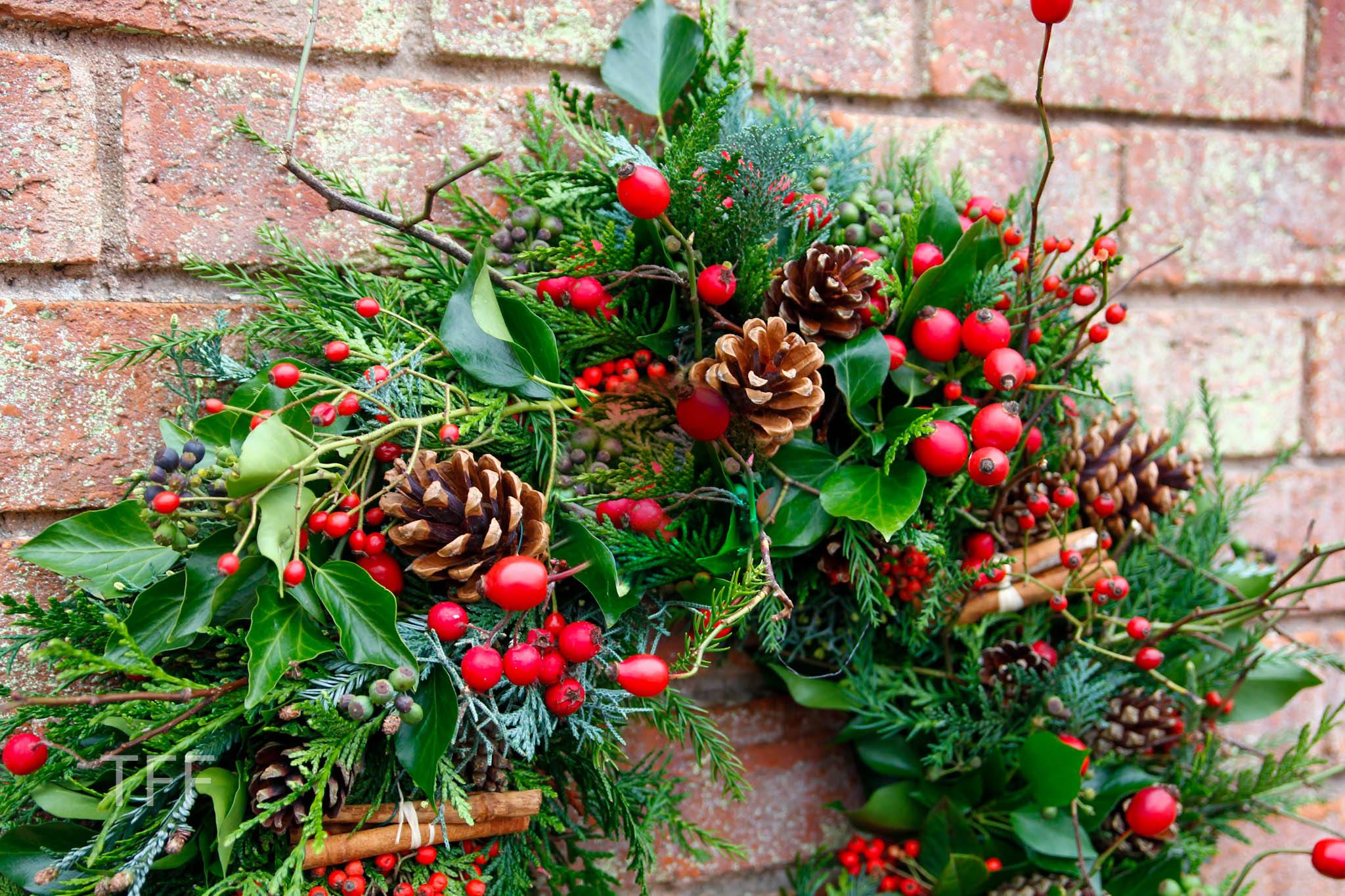 evergreen foliage on a table, with a pair of hands wearning blue gloves picking through it to attach it to a metal wreath ring.