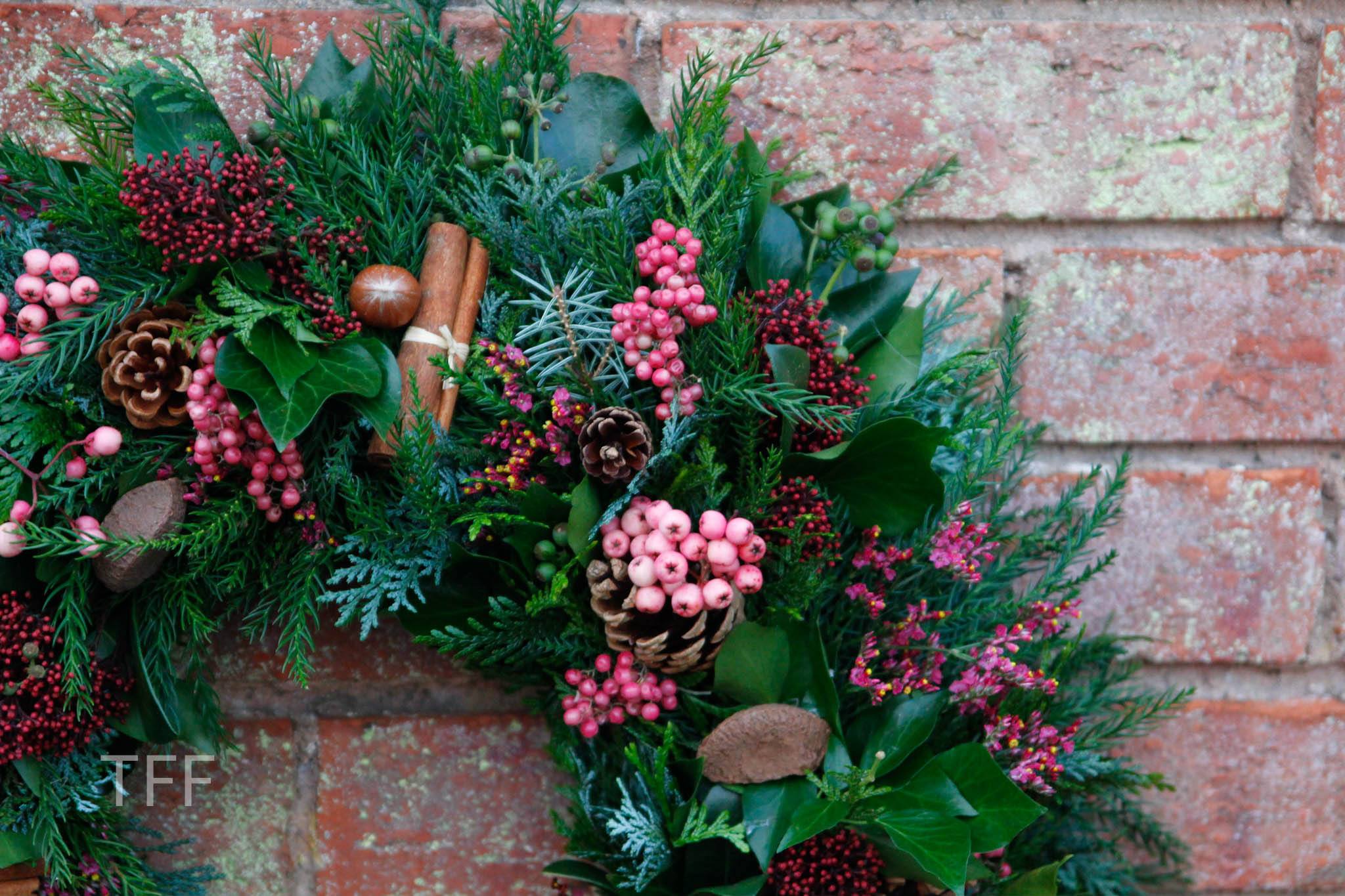 evergreen foliage on a table, with a pair of hands wearning blue gloves picking through it to attach it to a metal wreath ring.