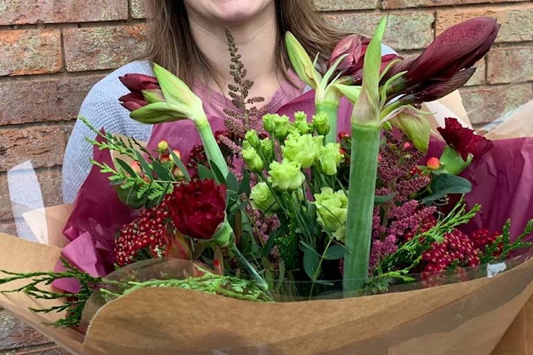 evergreen foliage on a table, with a pair of hands wearning blue gloves picking through it to attach it to a metal wreath ring.